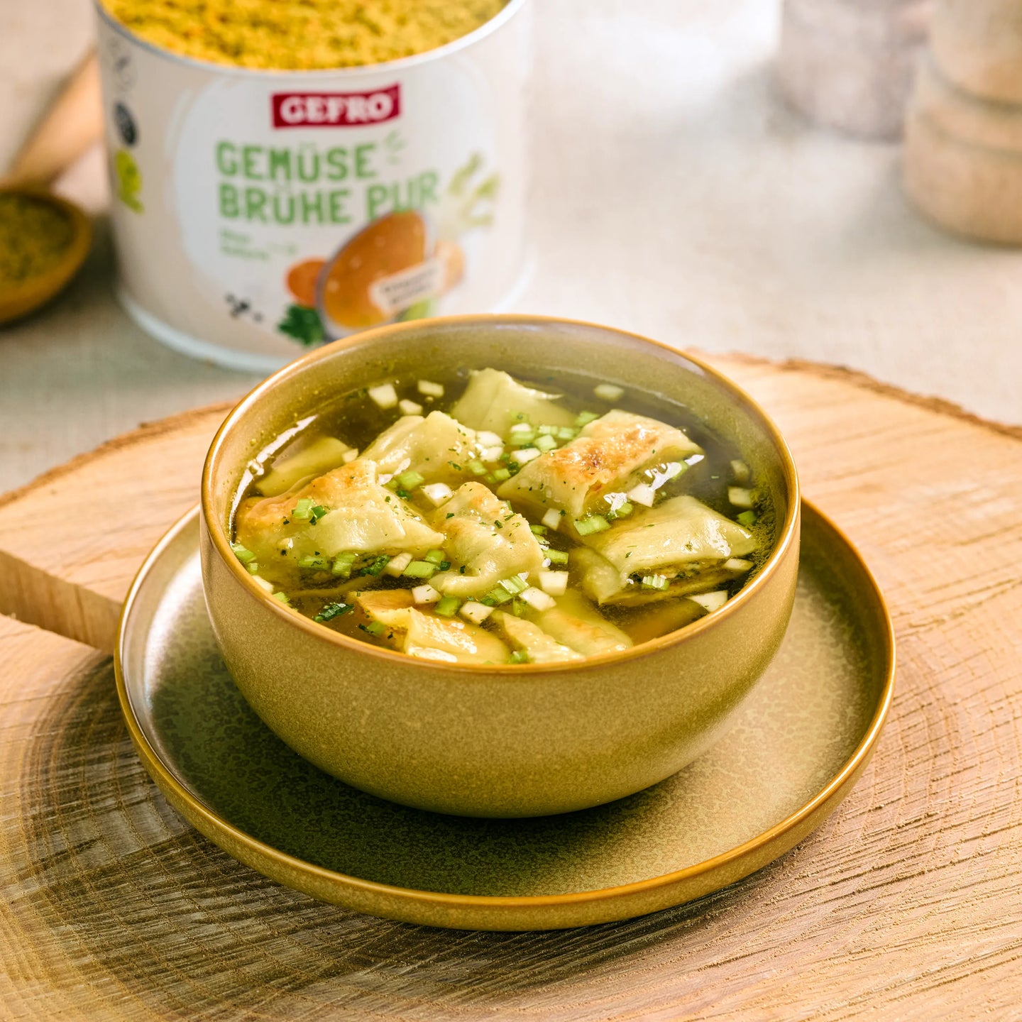 Schale mit klarer Gemüsesuppe und gefüllten Teigtaschen auf Holzbrett, im Hintergrund Dose Gemüsebrühe Pur von Gefro