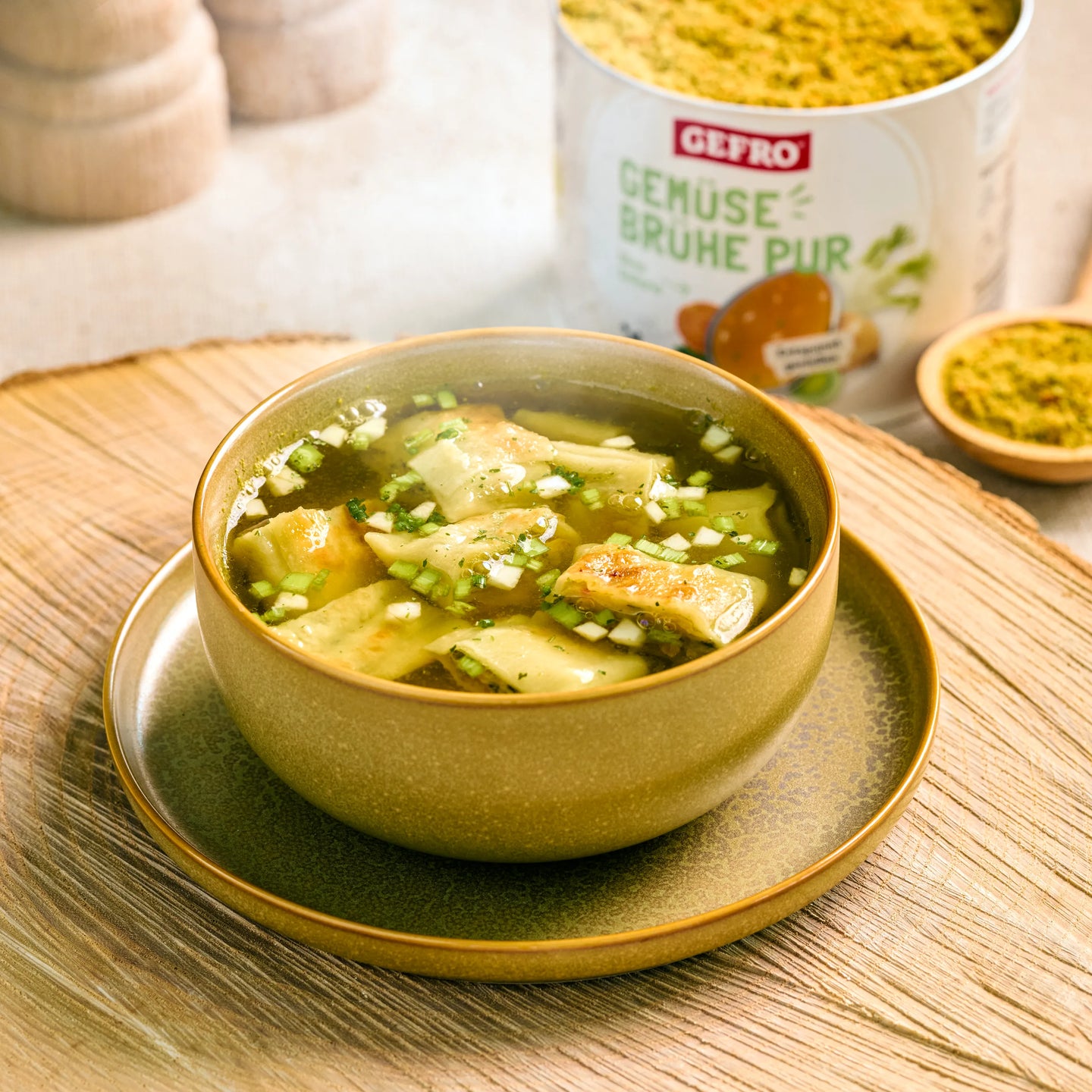 Schale mit klarer Gemüsesuppe und Teigtaschen auf einem Teller, daneben GEFRO Gemüsebrühe Pur im Hintergrund