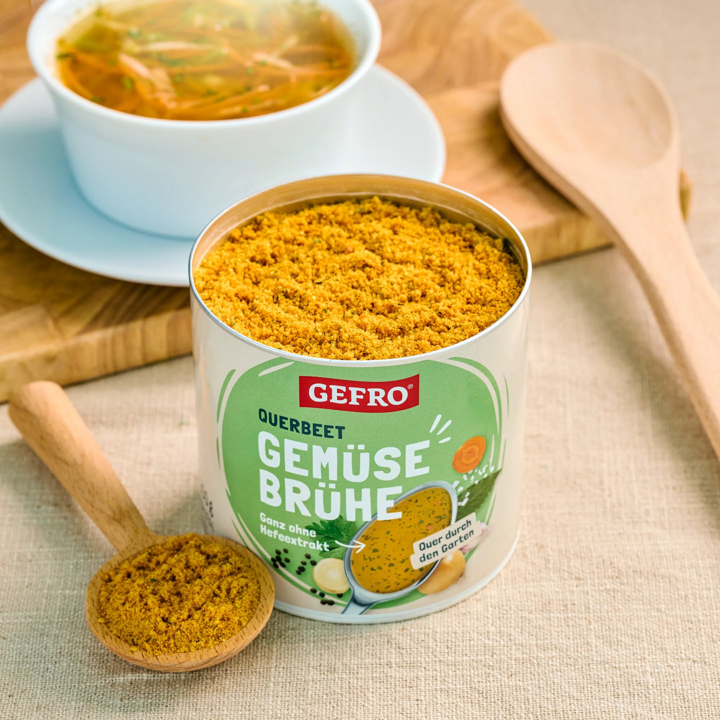 Offene Dose Gemüsebrühe von Gefro mit Löffel und fertiger Suppe in einer Schale auf hellem Tisch.