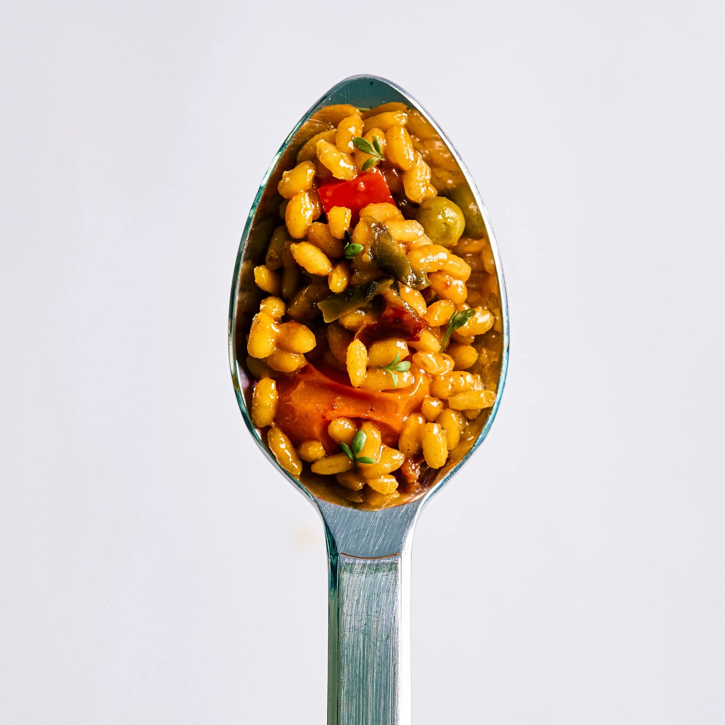 Löffel mit würzigem Getreidesalat aus Graupen, Paprika und Kräutern vor hellem Hintergrund in Nahaufnahme