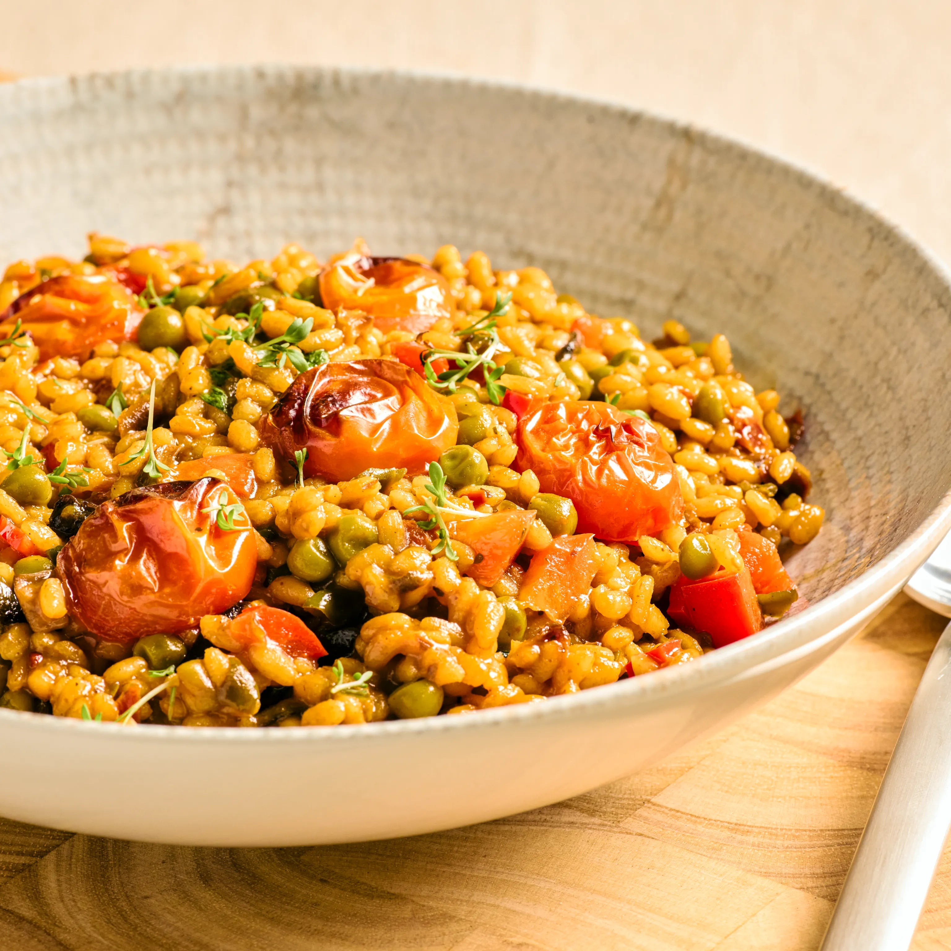 Schale mit Reisgericht aus Erbsen, gerösteten Tomaten und Paprika auf Holztisch, servierfertig angerichtet