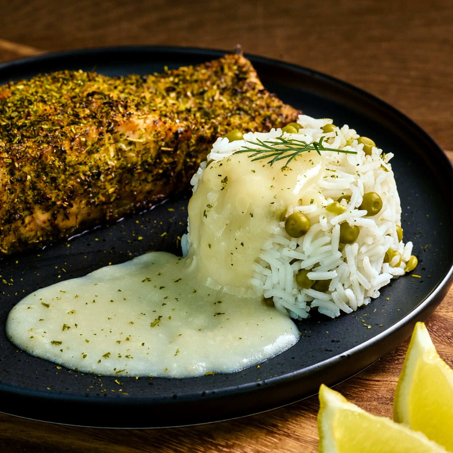Gewürztes Lachsfilet mit Reis und Erbsen, dazu helle Sauce auf schwarzem Teller, serviert mit Zitronenspalten