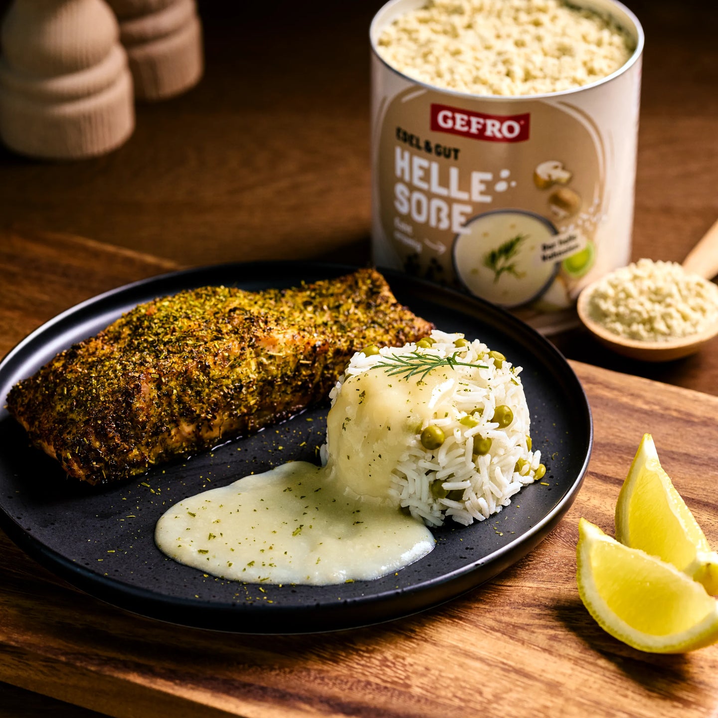 Gewürztes Fischfilet mit Reis, Erbsen und heller Soße auf schwarzem Teller, daneben Produktdose und Zitronenspalten