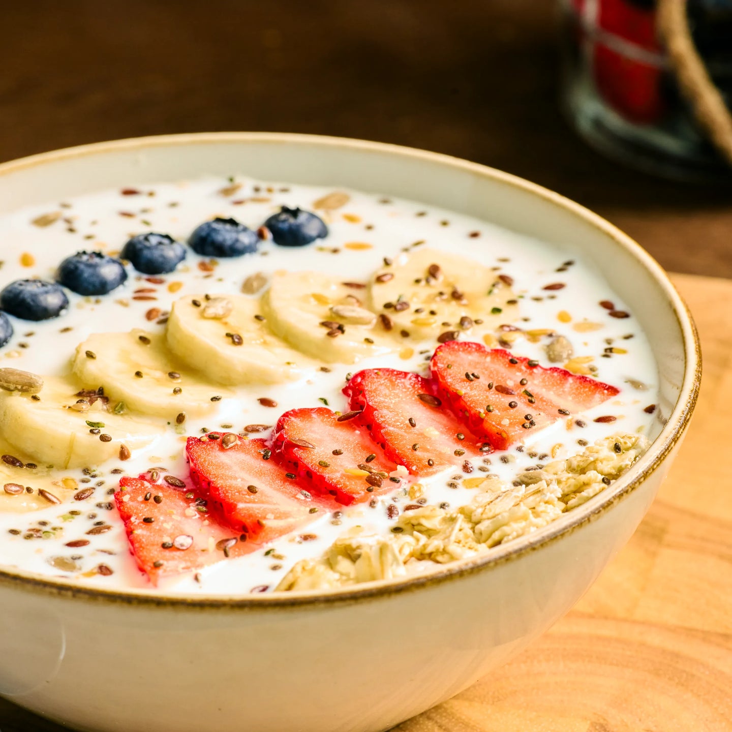 Schale mit Joghurt, Haferflocken, Bananen-, Erdbeer- und Blaubeerscheiben sowie Samen als Frühstück serviert