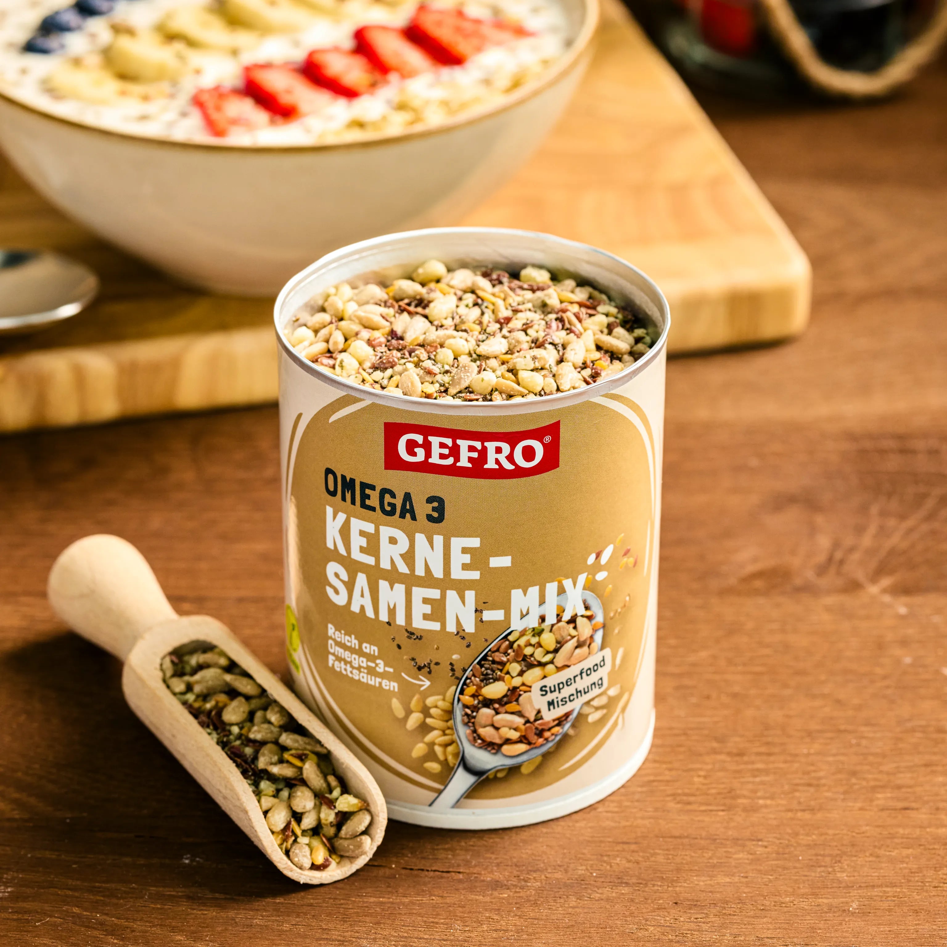 Dose GEFRO Omega 3 Kerne-Samen-Mix auf Holztisch, davor eine Schaufel mit Kernen, im Hintergrund eine Müslischale.