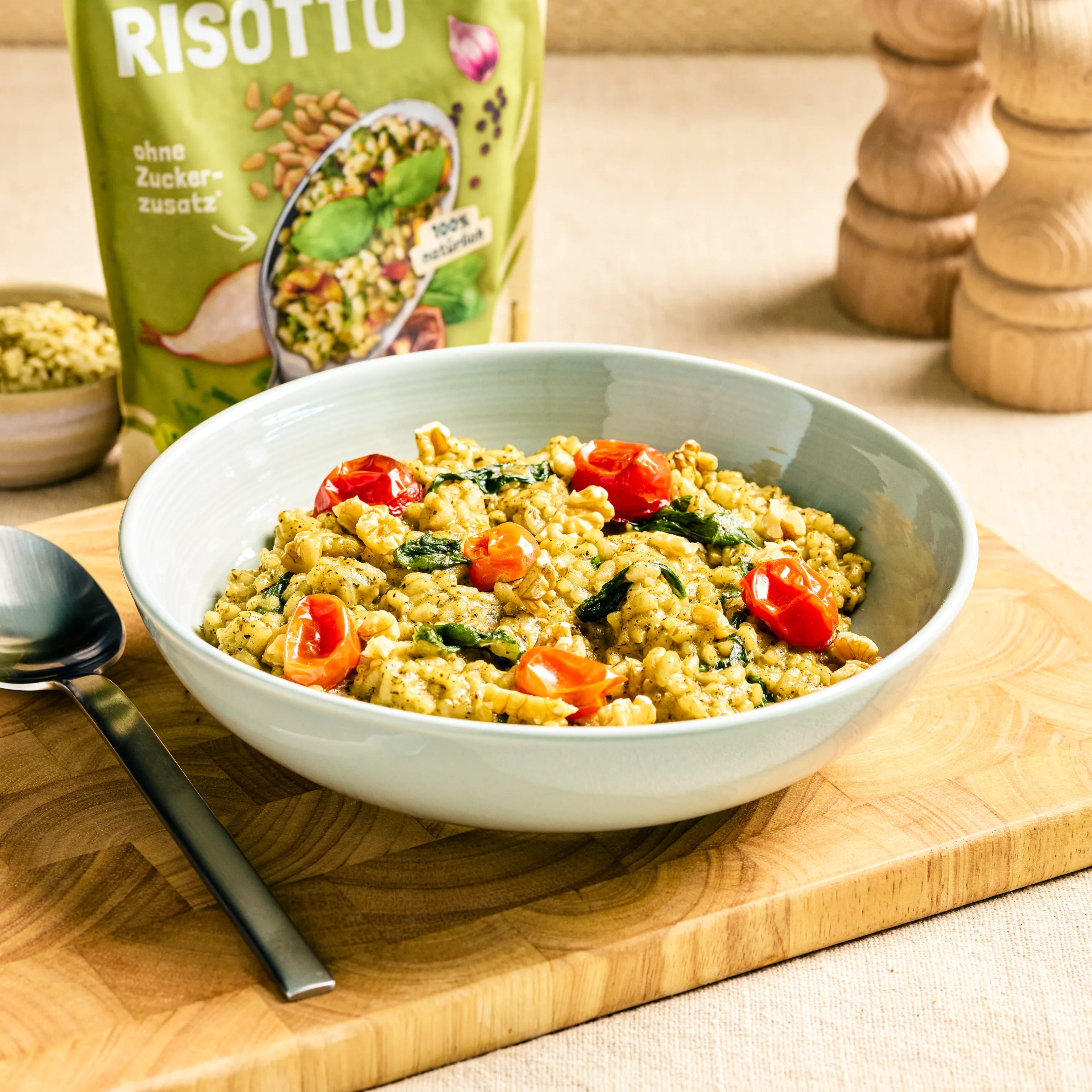 Schüssel mit cremigem Risotto mit Kirschtomaten und Spinat auf Holzbrett, dahinter die passende Produktverpackung