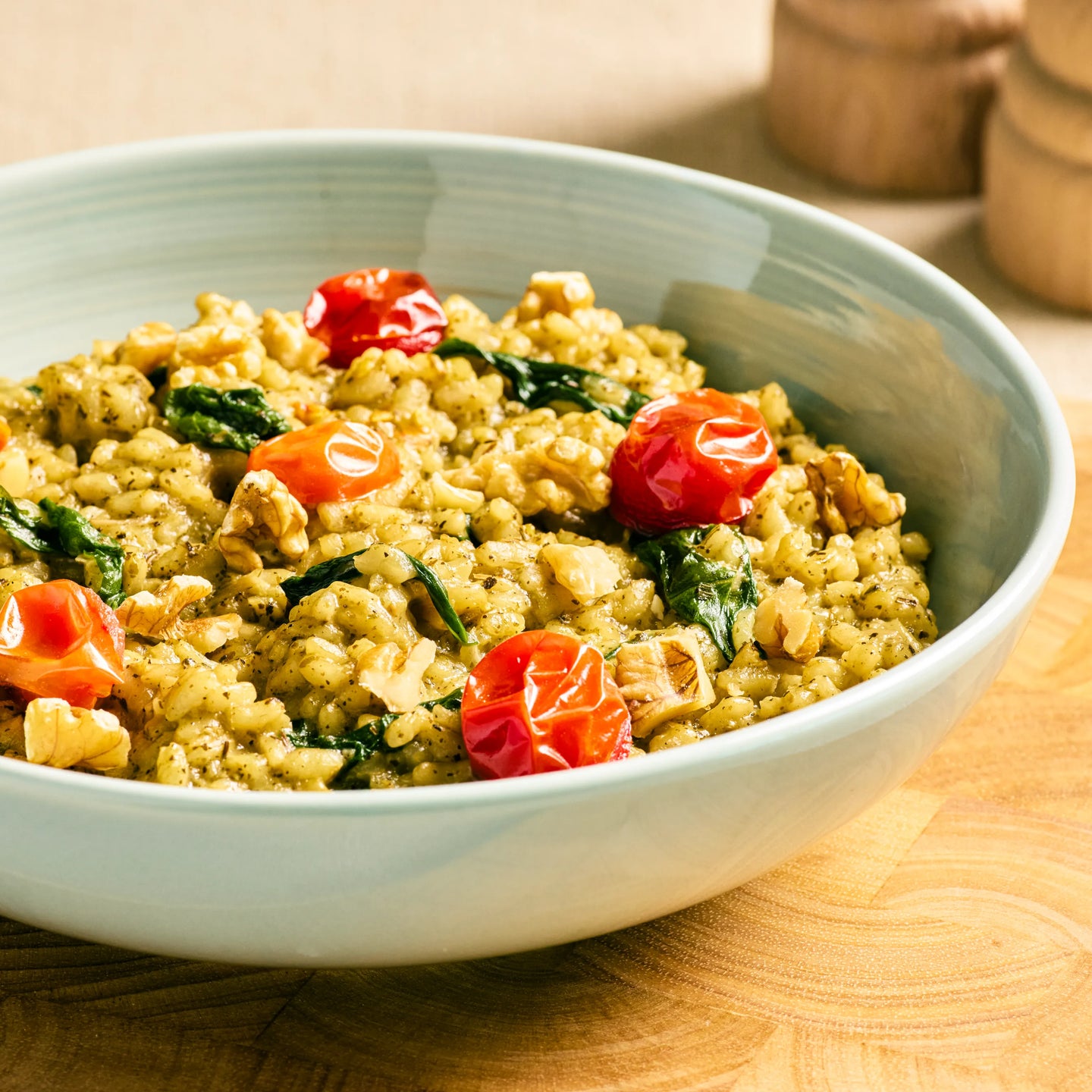 Schüssel mit cremigem Risotto, garniert mit Kirschtomaten, Spinat und Walnüssen auf hellem Holztisch