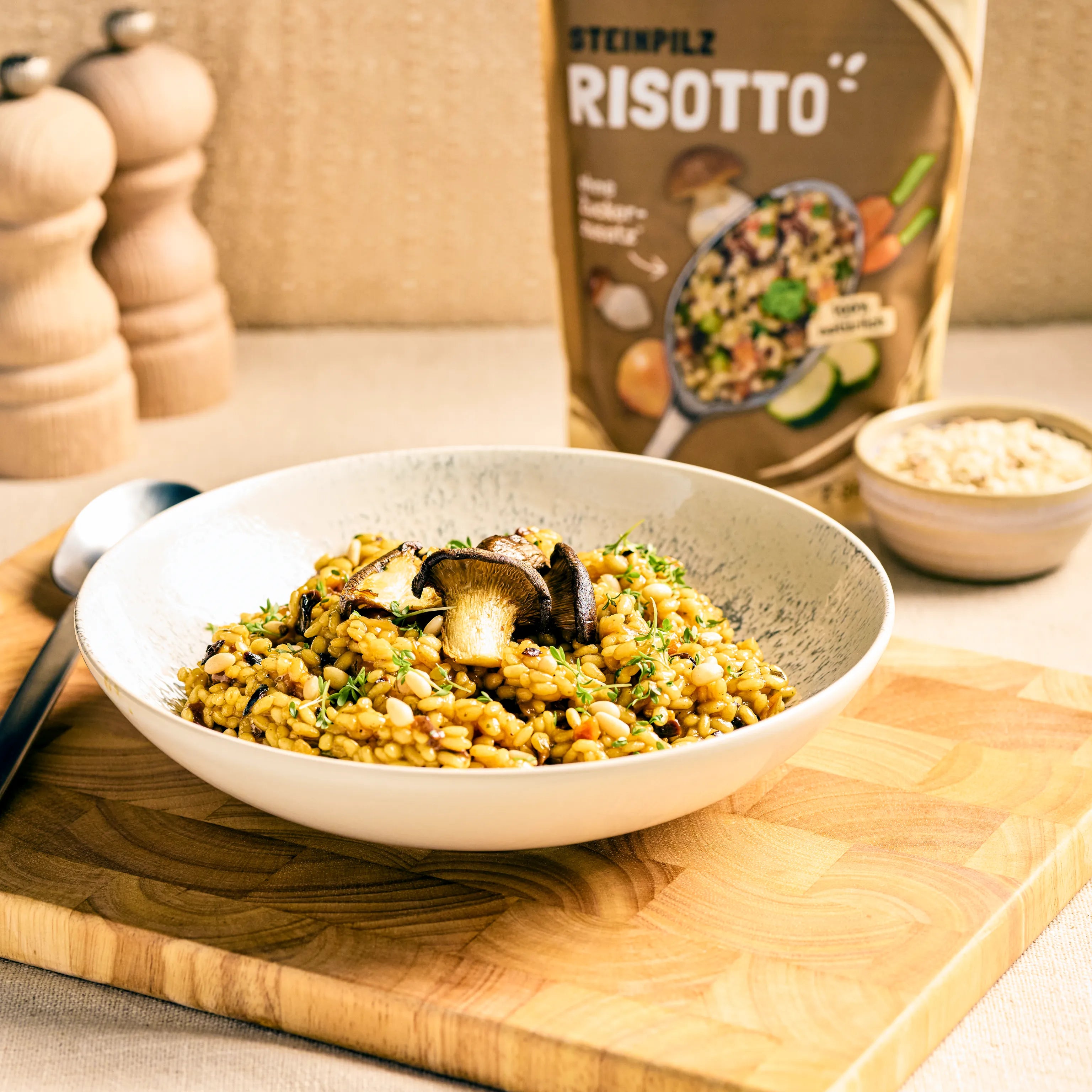 Schüssel mit Steinpilz-Risotto auf Holzbrett, garniert mit Pilzen; dahinter steht die passende Produktverpackung.