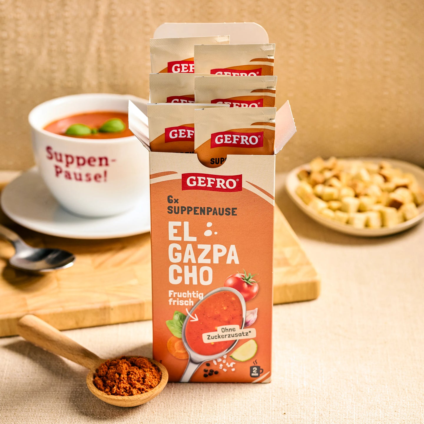 Offene Packung GEFRO Suppenpause El Gazpacho mit Portionsbeuteln, daneben Schale Suppe und Croutons auf dem Tisch