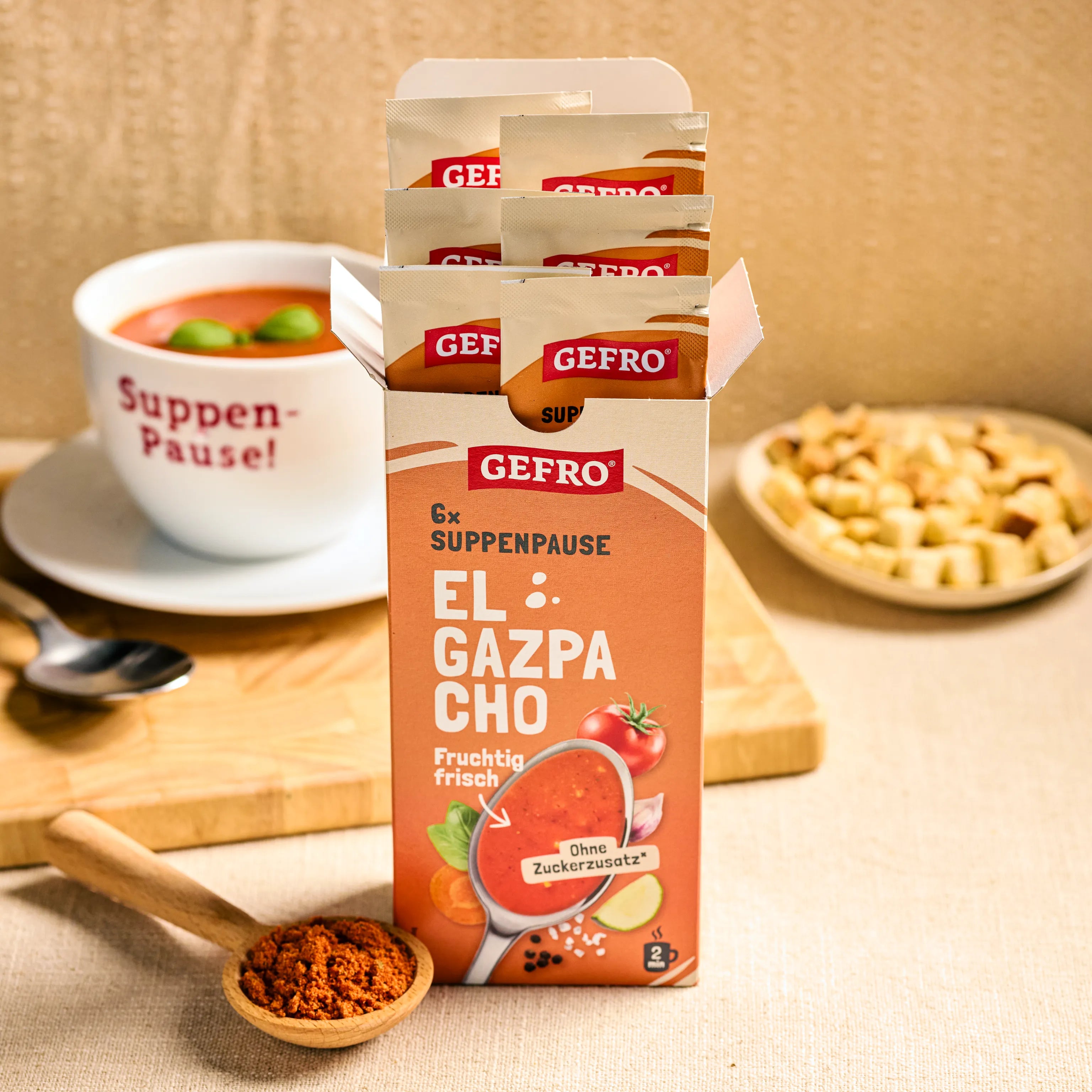 Offene Packung GEFRO Suppenpause El Gazpacho mit Portionsbeuteln, daneben Schale Suppe und Croutons auf dem Tisch