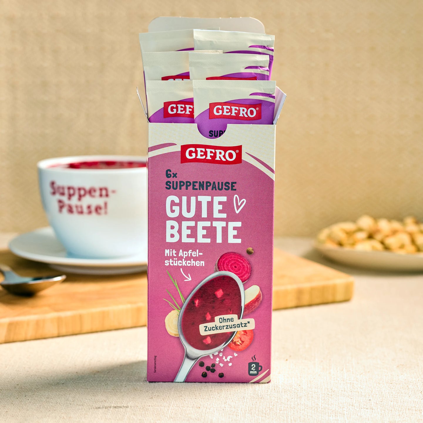 Geöffnete Packung GEFRO Suppenpause Gute Beete mit Portionsbeuteln, daneben Tasse und Snack im Hintergrund