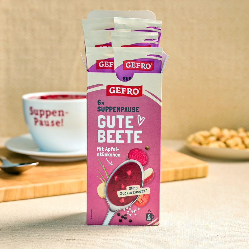 Geöffnete Packung GEFRO Suppenpause Gute Beete mit Portionsbeuteln, daneben Tasse und Snack im Hintergrund