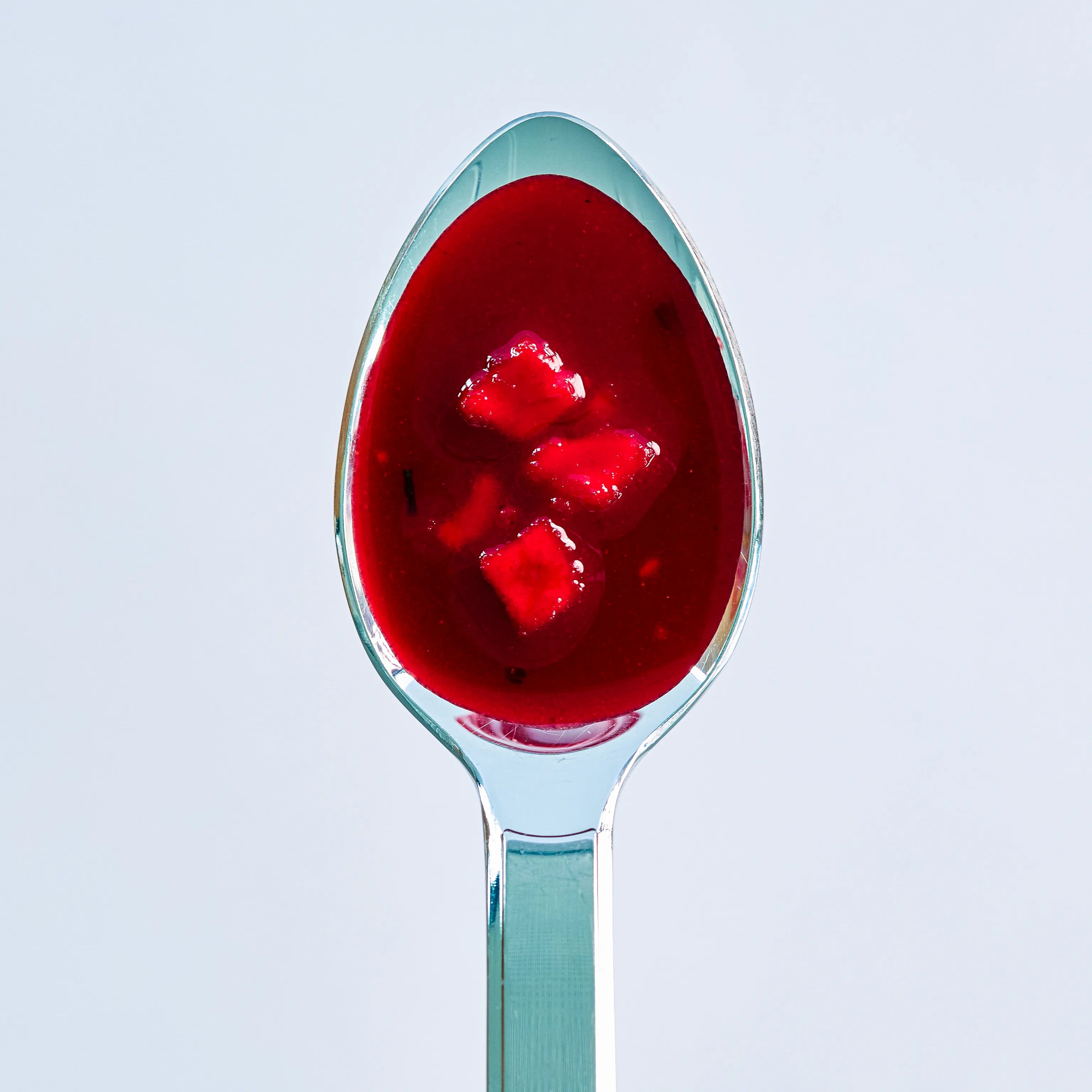 Löffel mit roter Fruchtsauce und kleinen Fruchtstücken vor hellem Hintergrund, appetitlich präsentiert