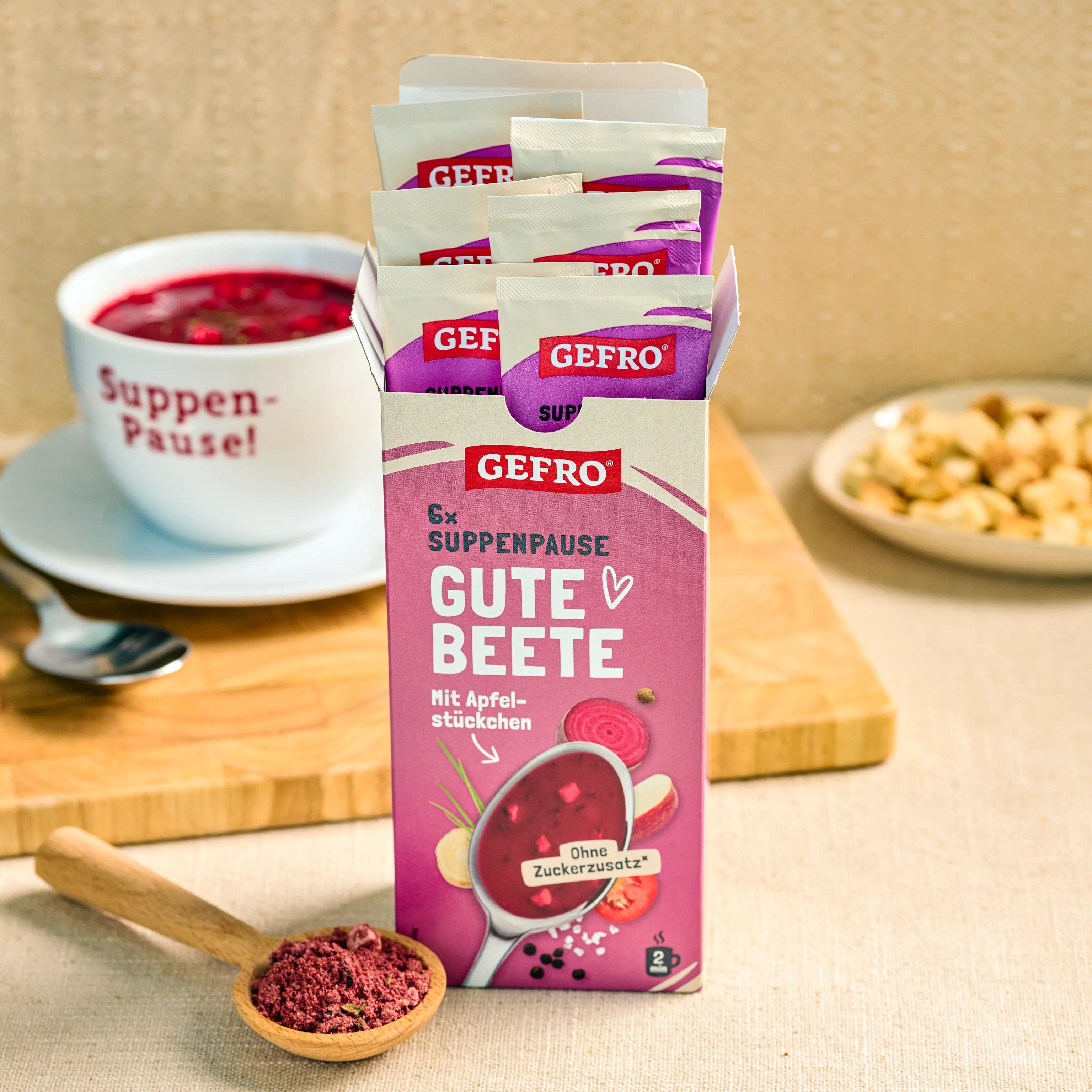 GEFRO Suppenpause Gute Beete mit Apfelstückchen in geöffneter Packung, daneben rote Suppe und Pulver im Holzlöffel