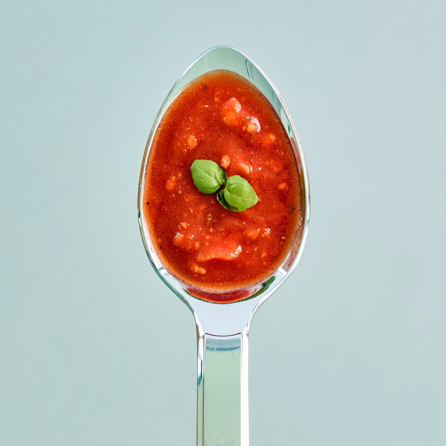 Löffel mit roter Tomatensauce und Basilikumblatt, nah aufgenommen vor hellem Hintergrund zur ansprechenden Präsentation
