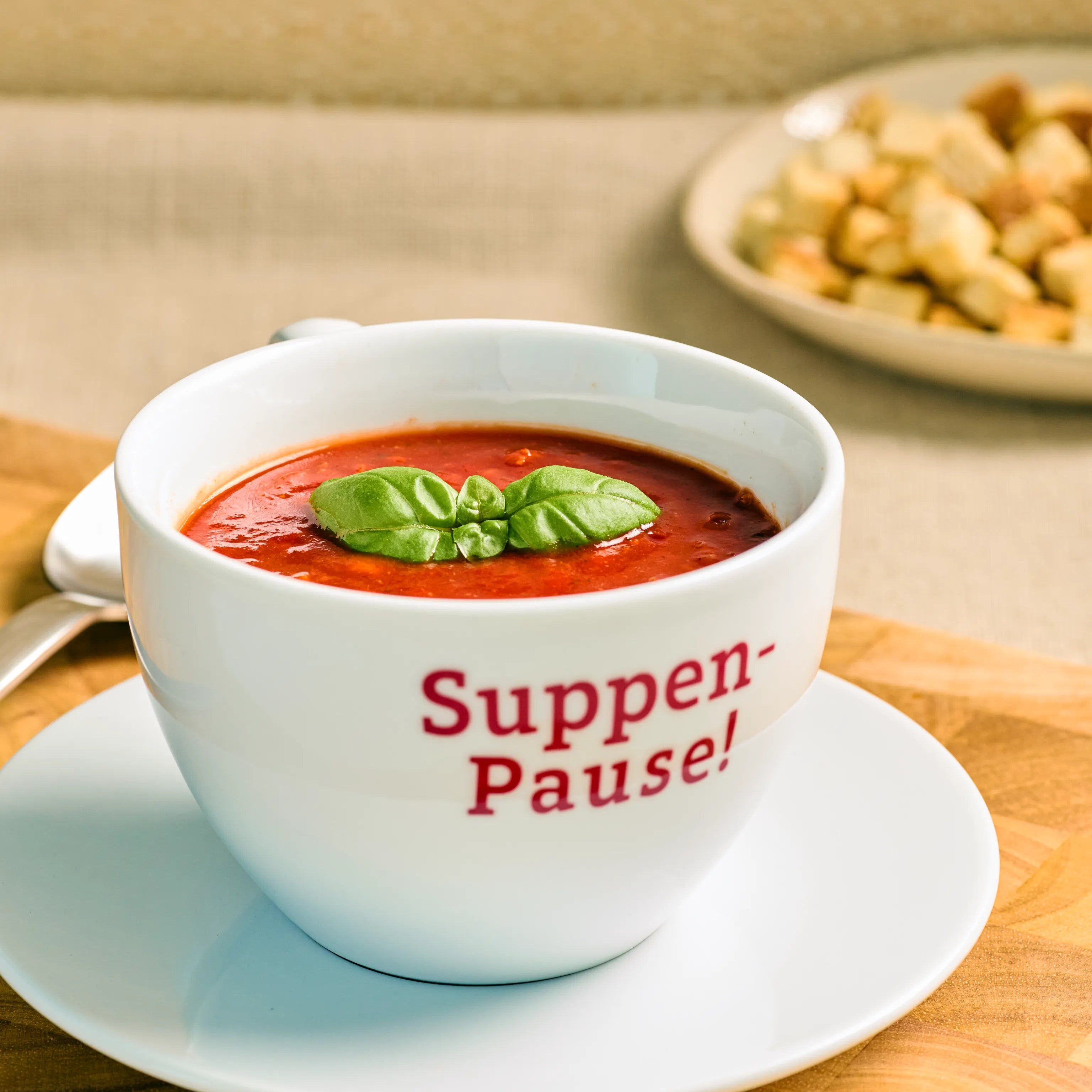 Weiße Suppentasse mit Tomatensuppe und Basilikum auf Untertasse, Aufdruck „Suppen-Pause!“, ideal zum Servieren