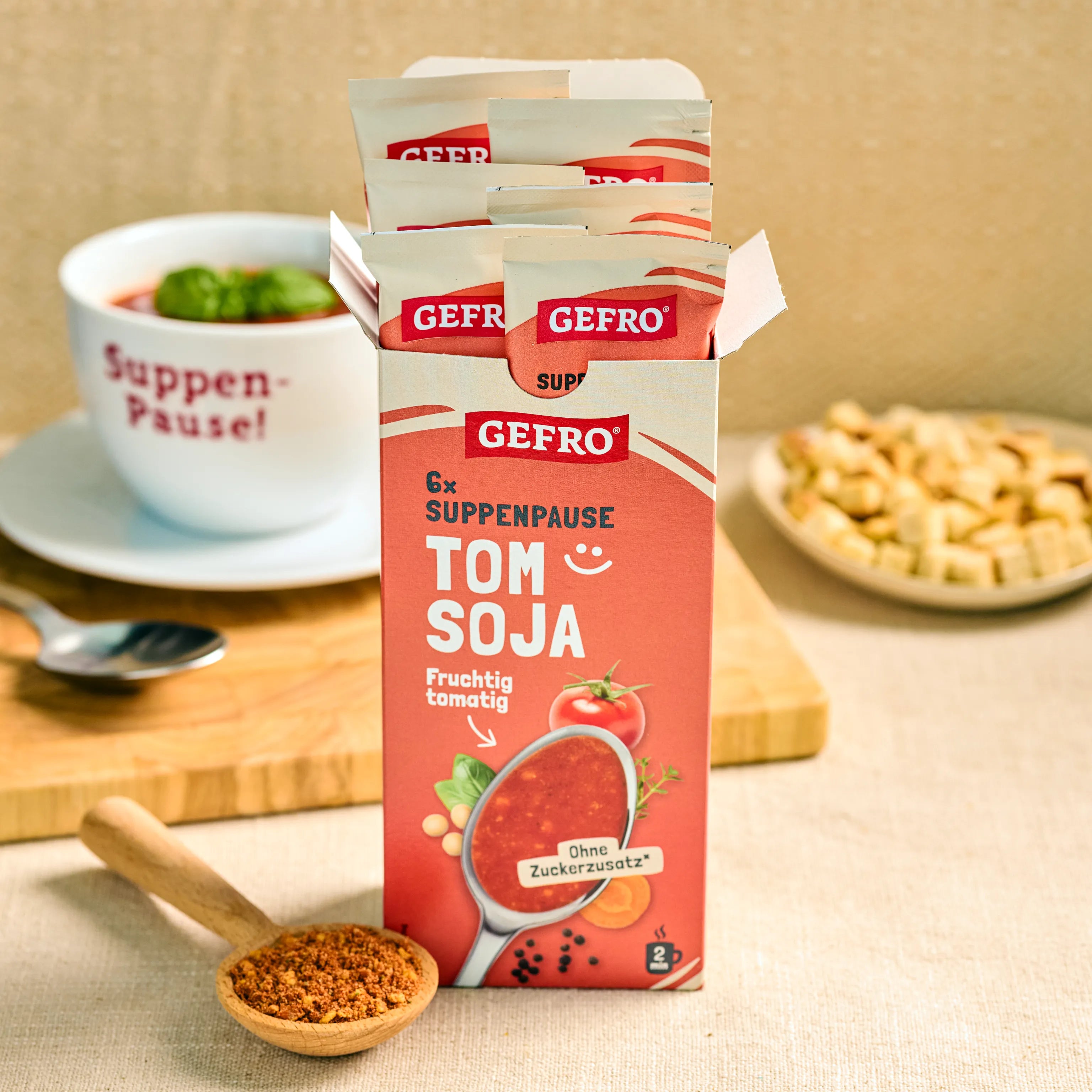 GEFRO Suppenpause Tom Soja in geöffneter Packung mit Portionsbeuteln, daneben Tasse Suppe und Gewürzlöffel