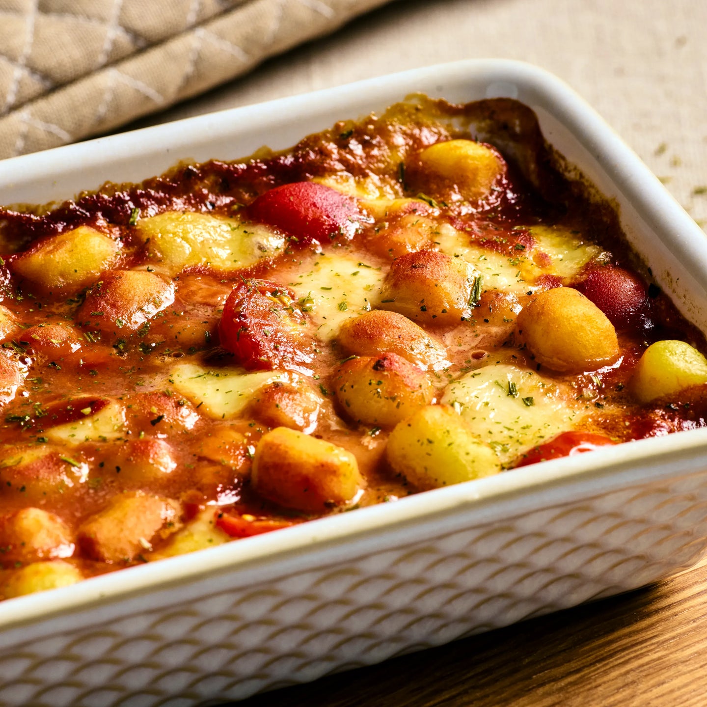Weiße Auflaufform mit überbackenen Gnocchi in Tomatensauce, geschmolzenem Käse und roten Tomatenstücken