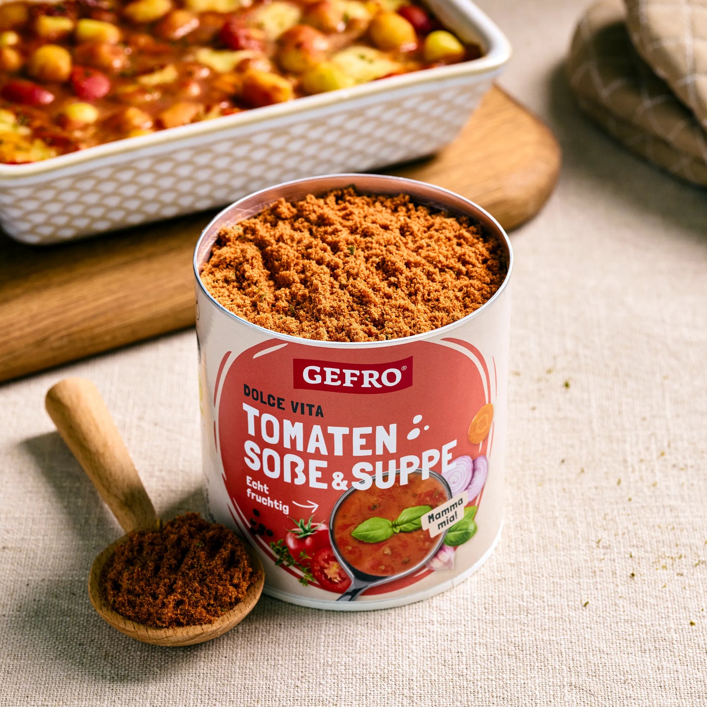 Dose mit GEFRO Tomaten Soße & Suppe Pulver und Holzlöffel, daneben ein Ofengericht im Hintergrund