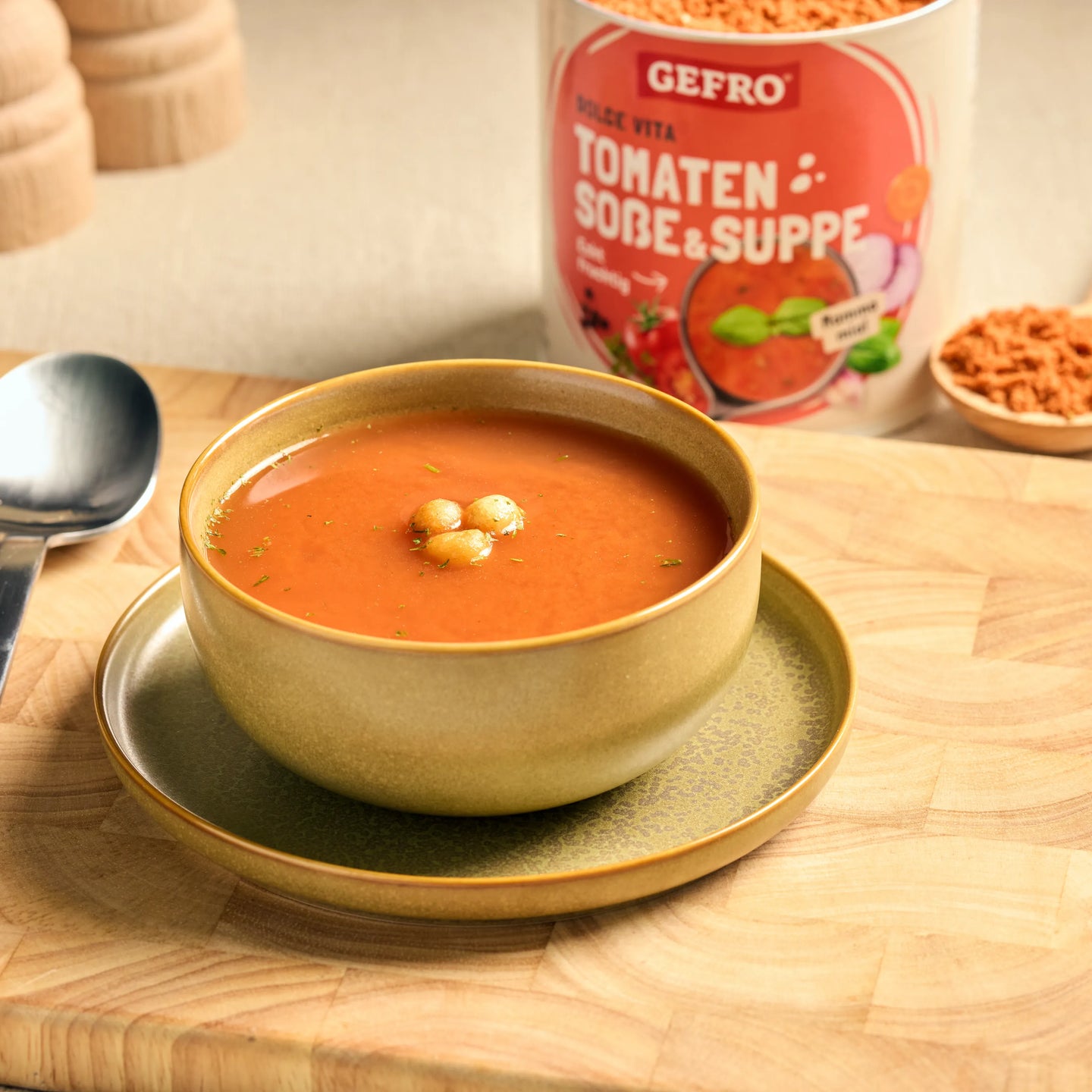 Schale mit Tomatensuppe auf Unterteller, im Hintergrund Packung GEFRO Tomaten Soße & Suppe auf Holztisch